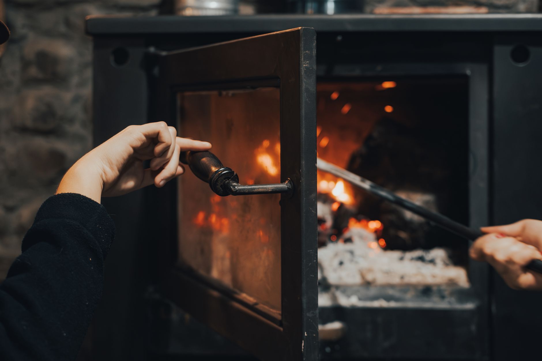 Hands tending to a warm, burning fireplace indoors, capturing the essence of comfort.